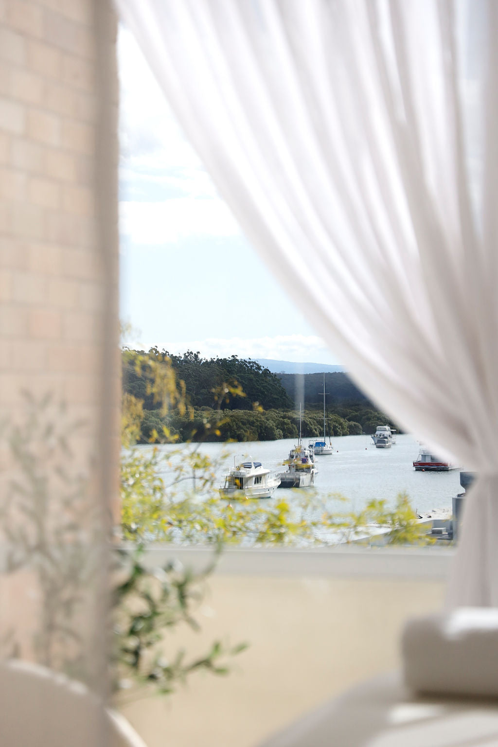 
This serene image captures a scenic view of boats gently floating on a calm bay, framed by lush greenery and soft, flowing white curtains. The composition evokes a peaceful, spa-like atmosphere, blending natural beauty with relaxation and tranquility.